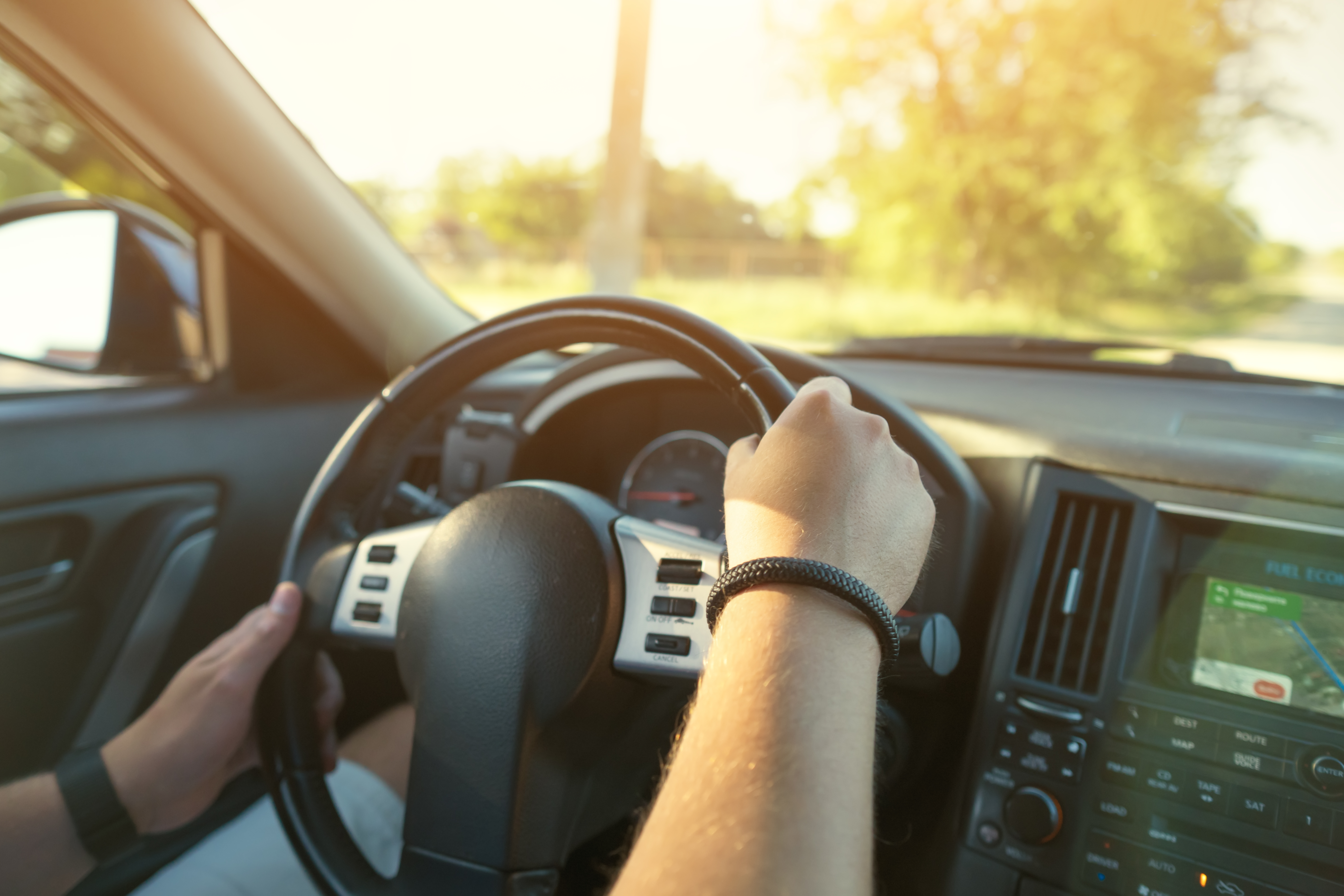 Driver’s hands on the steering wheel of the car and dashboard.